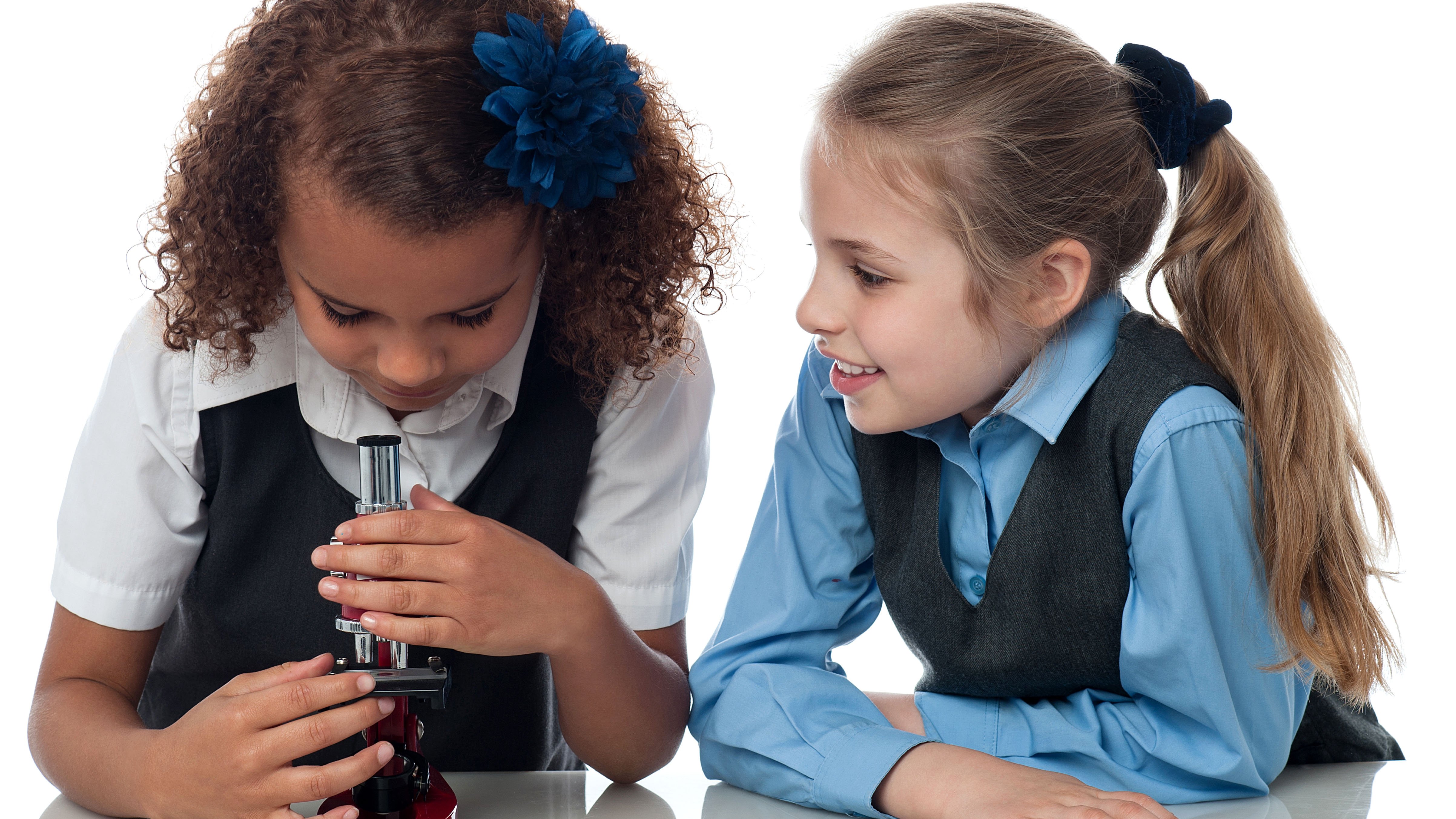 Two school girls, one looking in a microscope while the other watches her smiling