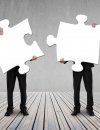 Two people holding two large puzzle pieces that appear to match as they begin to connect them