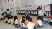 Male teacher sitting on mat in front of a class full of small kids