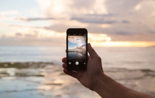 Hand holding a phone with a picture of the beach in front of it on the phone